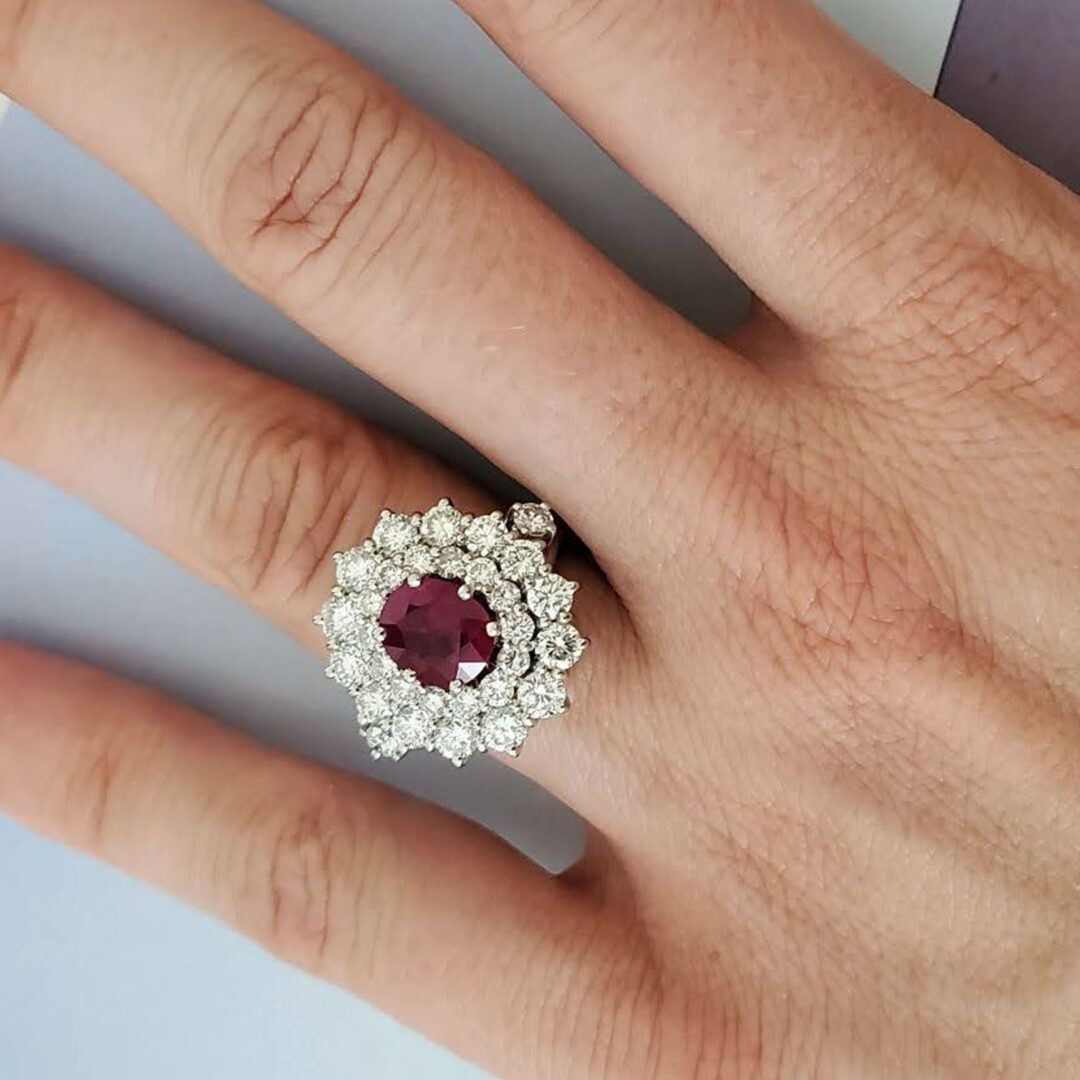 Sortija tipo solitario realizada en oro blanco de Ley, que tiene como protagonista un centro de rubí natural talla oval de 2 cts. de peso decorado por roseta de diamantes naturales talla brillante.